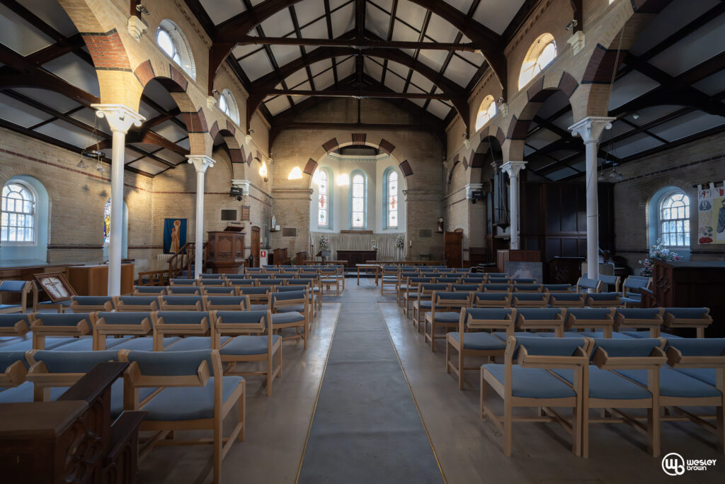 Broadmoore Hospital_3 Interior of a historical chapel with wooden pews and arched windows.